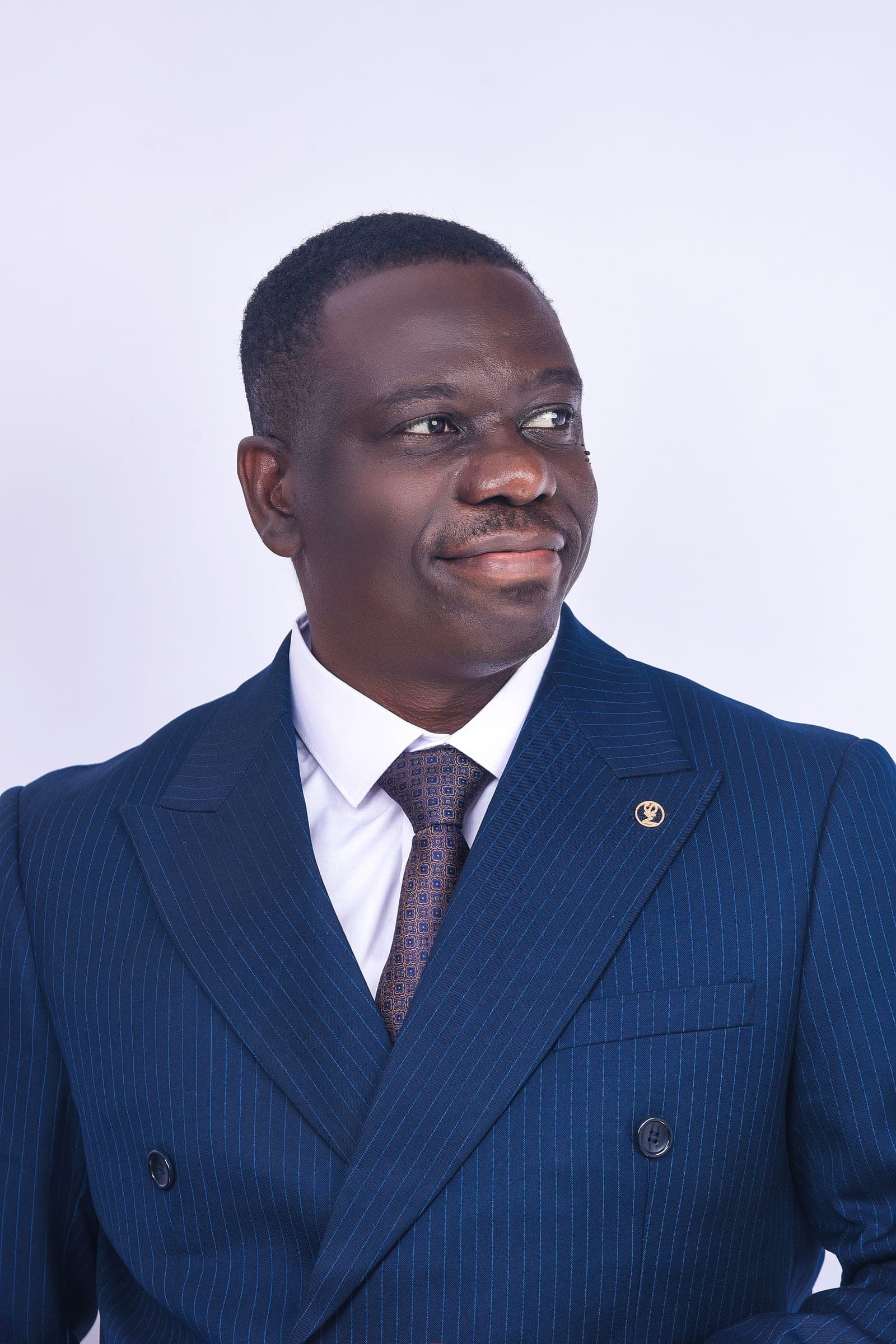 Raphael Amponsah in a navy pinstripe suit, looking to the side